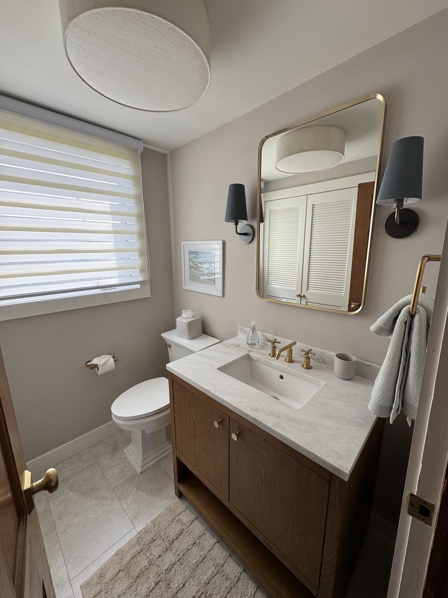 Powder bathroom after renovation — marble-top vanity and brass mirror