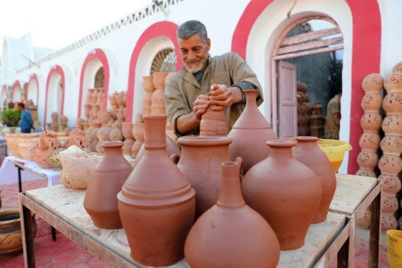A potter shaping a clay vessel among terracotta pots